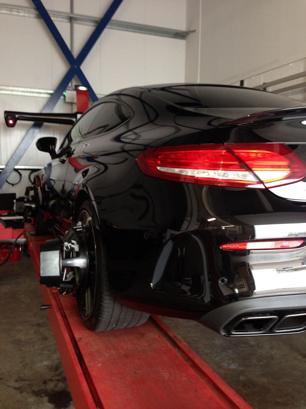 A black Mercedes on the ramp with alignment clamps on the rear wheel